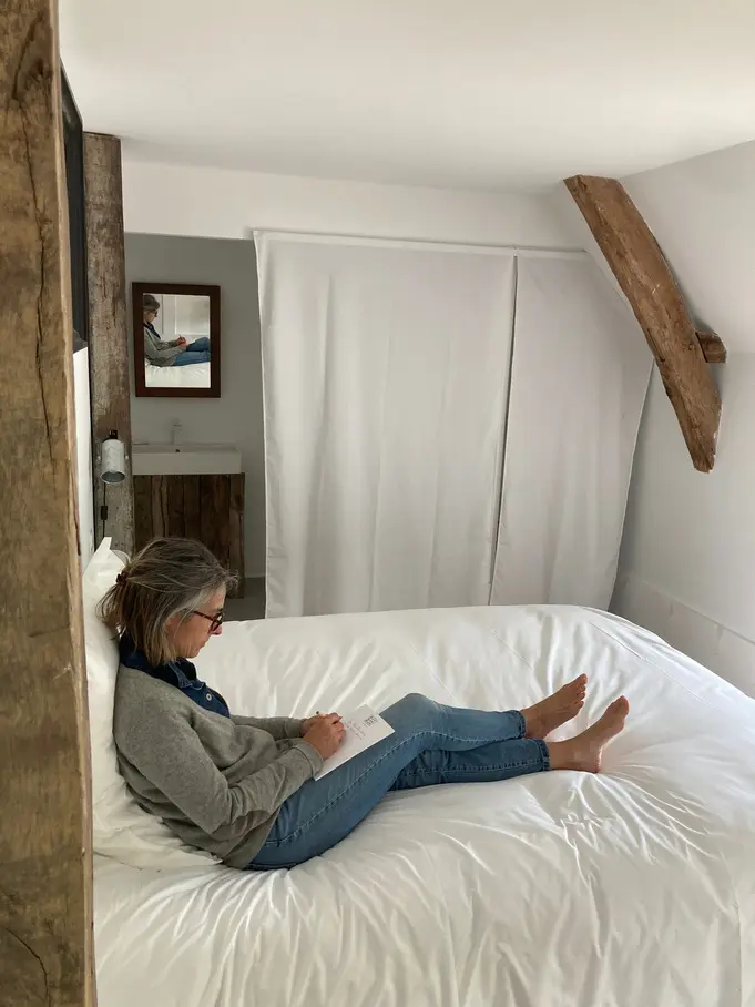 A guest reading on a white bed under old oak beams