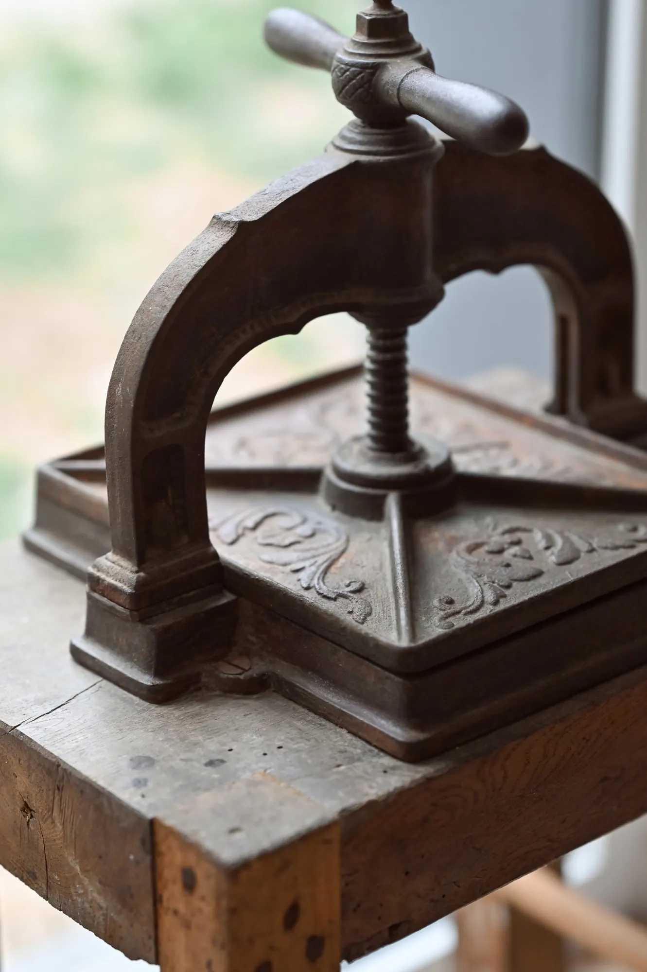 An antique cast-iron press on a wooden bench by a window