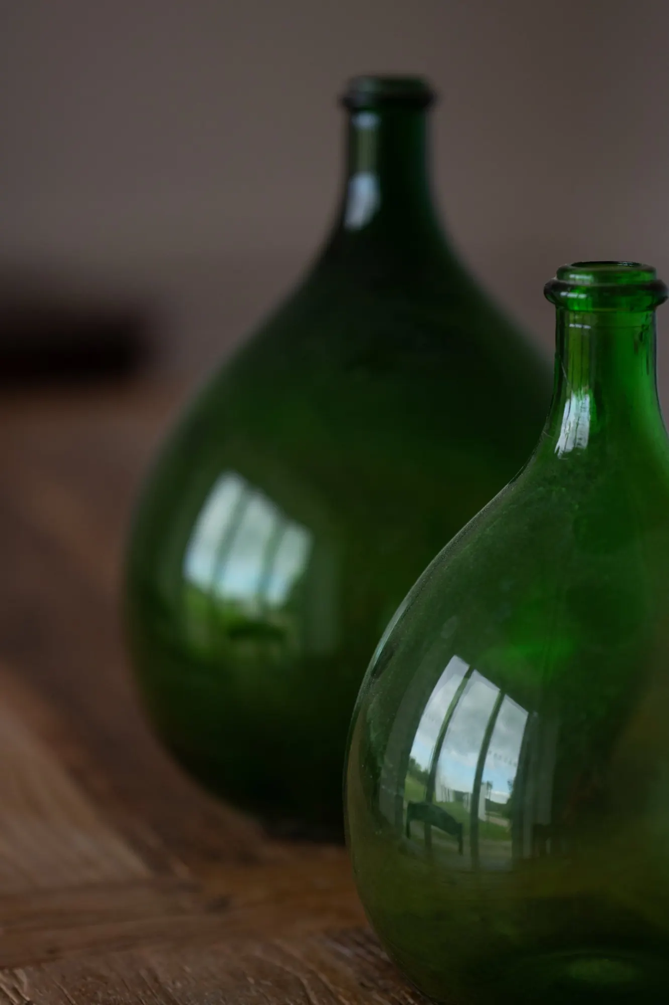 Two green glass demijohns on an oak table