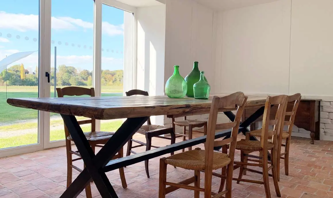 Salle à manger du Magasin avec une table en bois et des carafes vertes devant le jardin