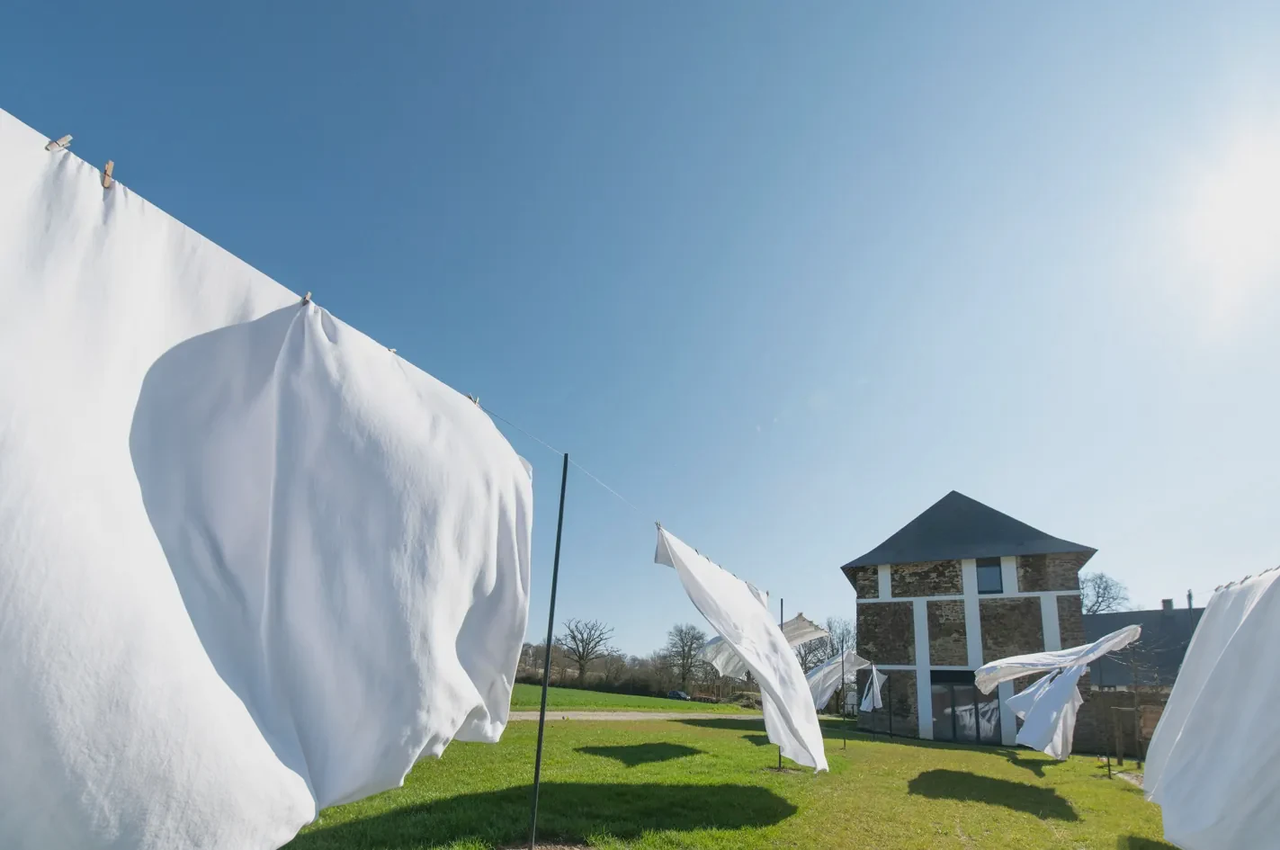 White sheets blowing on the lines under a blue sky, in front of the stone house