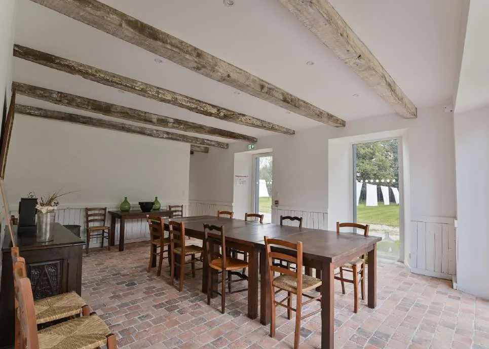 Salle à manger du Teinturier sous les poutres, avec sol en briques et portes ouvertes sur le parc