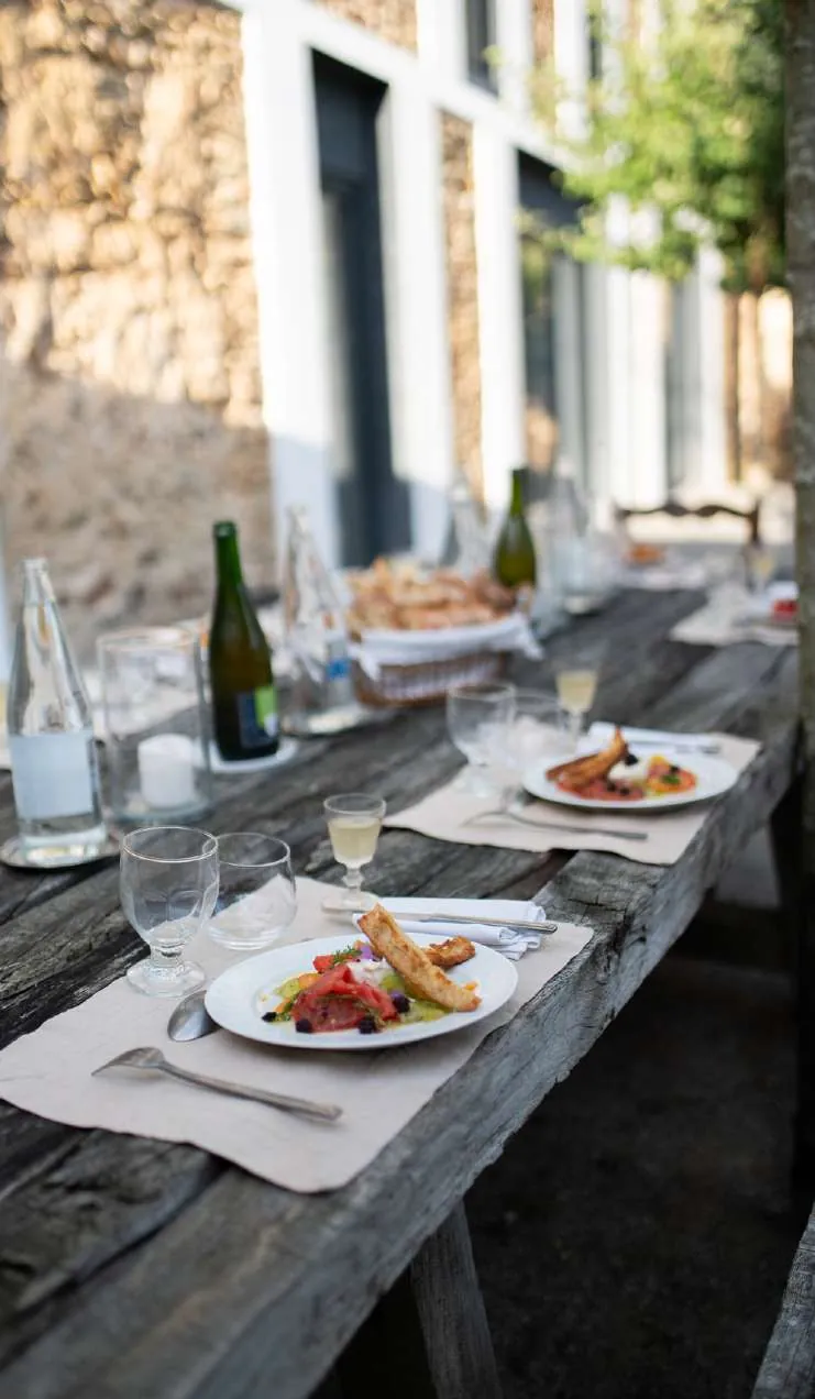 Table en vieux bois dressée dans la cour, avec assiettes de saison et verres